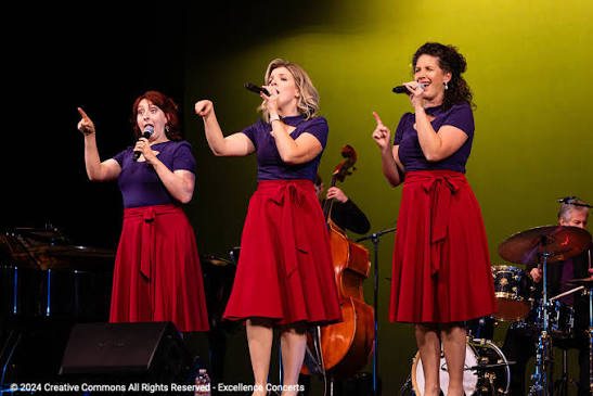 Trio de chanteuses sur scène avec ensemble instrumental